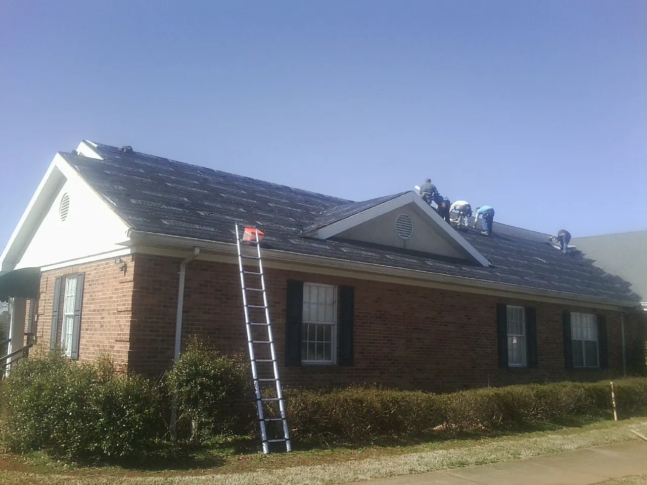 Crew tearing shingles off a brick ranch roof with a ladder set — Emergency Roof Repair work by our crew in Countyline