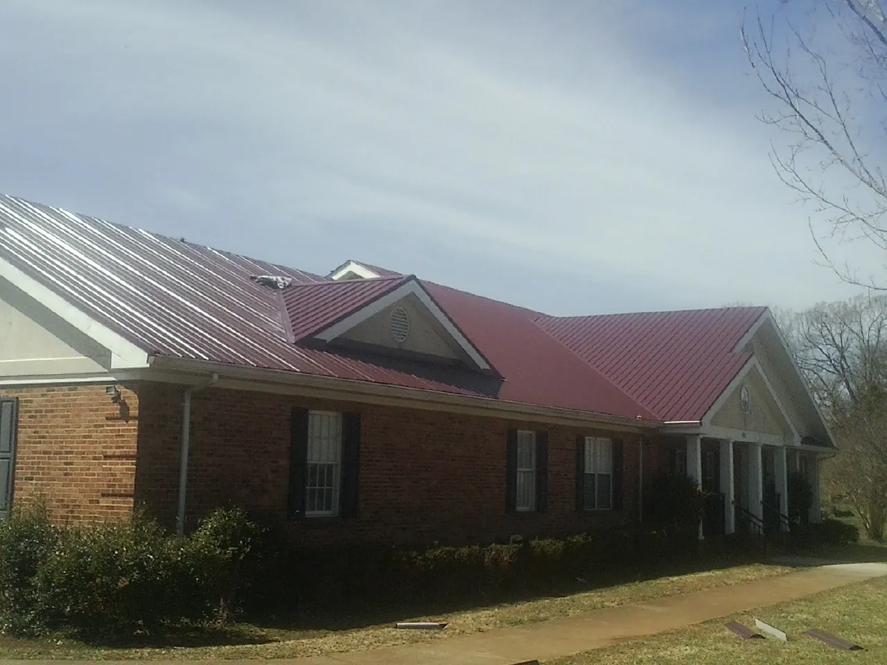Red metal roof with gabled entries on a long brick building, from a Hail Damage Roof Repair job in Countyline