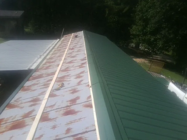 Old rusted panels beside newly installed green metal roofing — Wind Damage Roof Repair by Roofing Brothers in Countyline