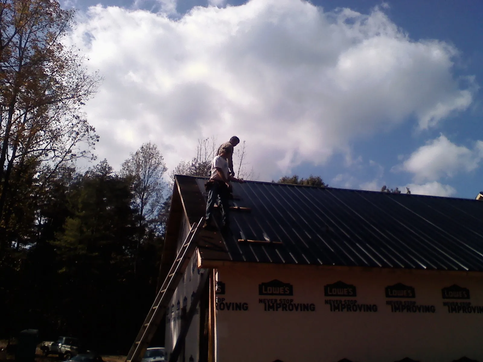 Roofer fastening dark metal panels high against a cloudy sky, from a Roof Inspection job in Countyline