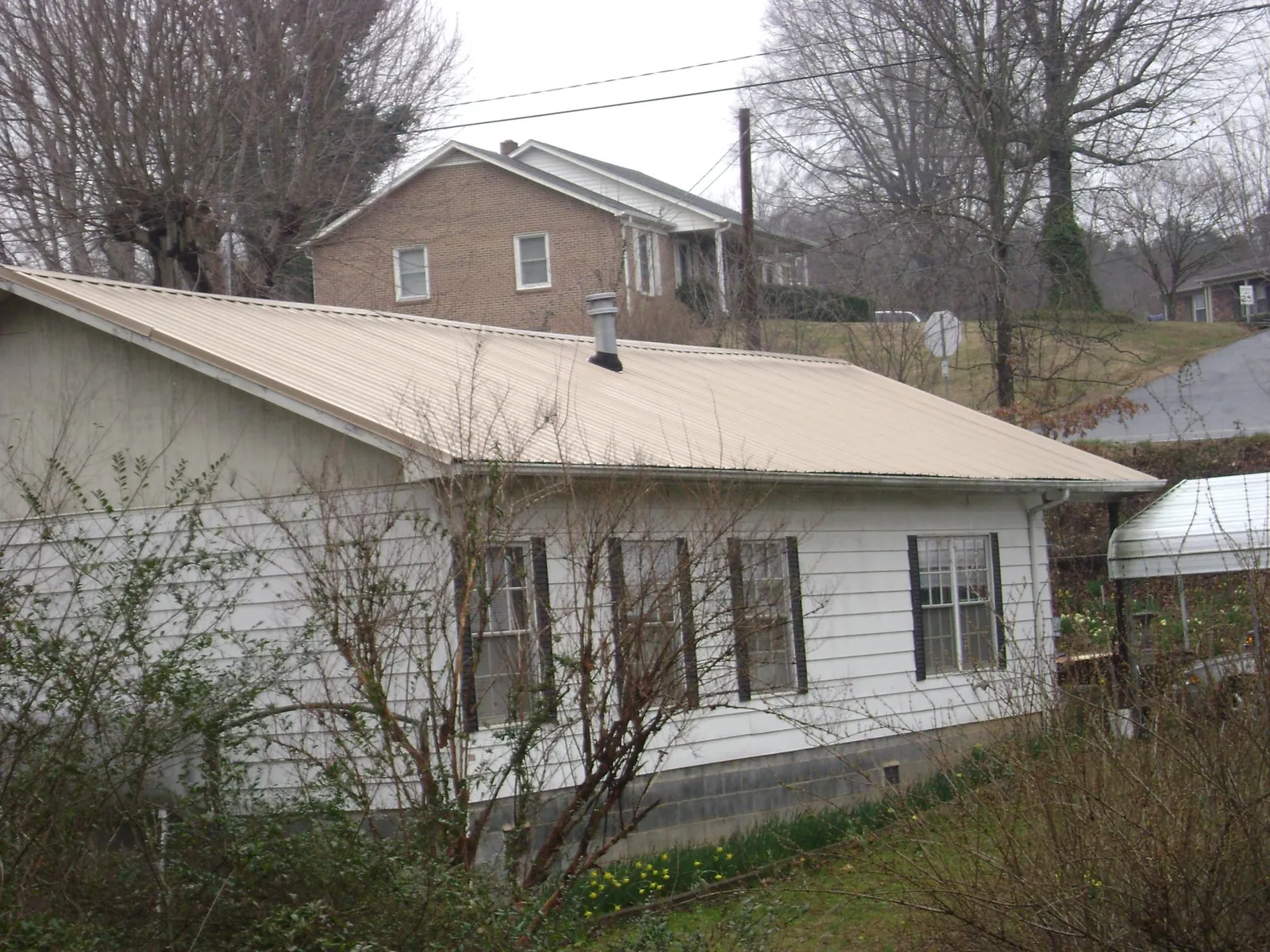 Tan metal roof on a white sided house set into a hillside — Commercial Roofing by Roofing Brothers in Countyline