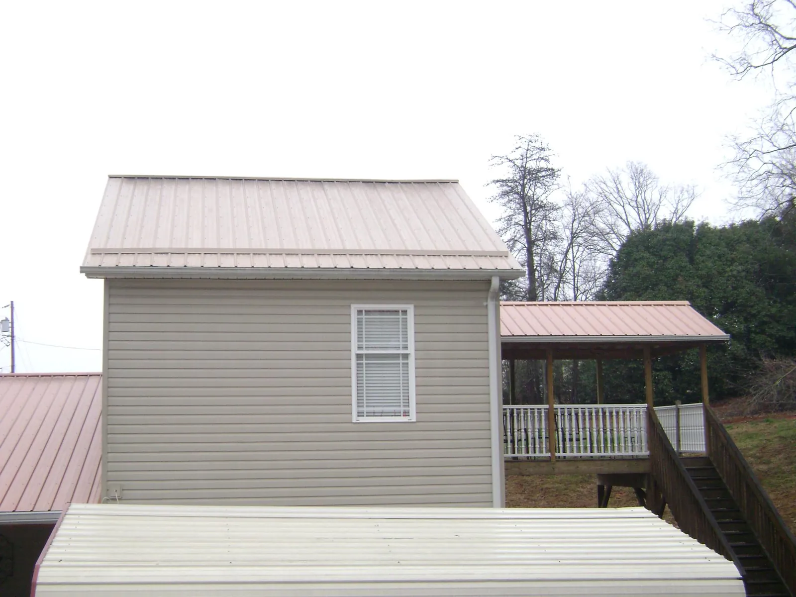 Tan metal roofs on a two story addition and attached porch, from a Roof Replacement job in Countyline